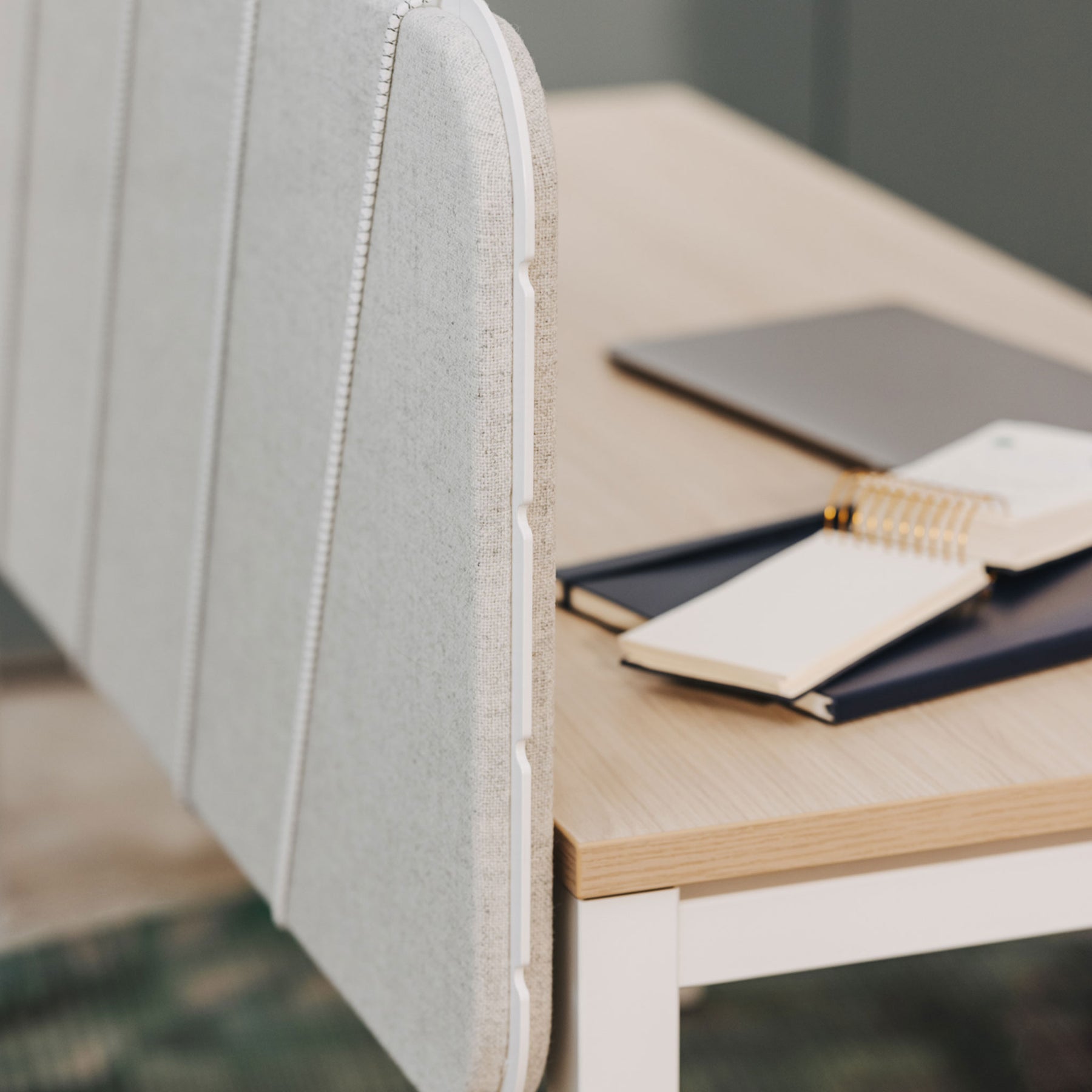 Man sieht in Nahaufnahme einen Arbeitsplatz mit Holz-Tischplatte und der Pinnwand in grauem Stoff und weißer Umrandung. Die Flexbänder sind weiß. Auf dem Tisch liegen mehrere Notizbücher.