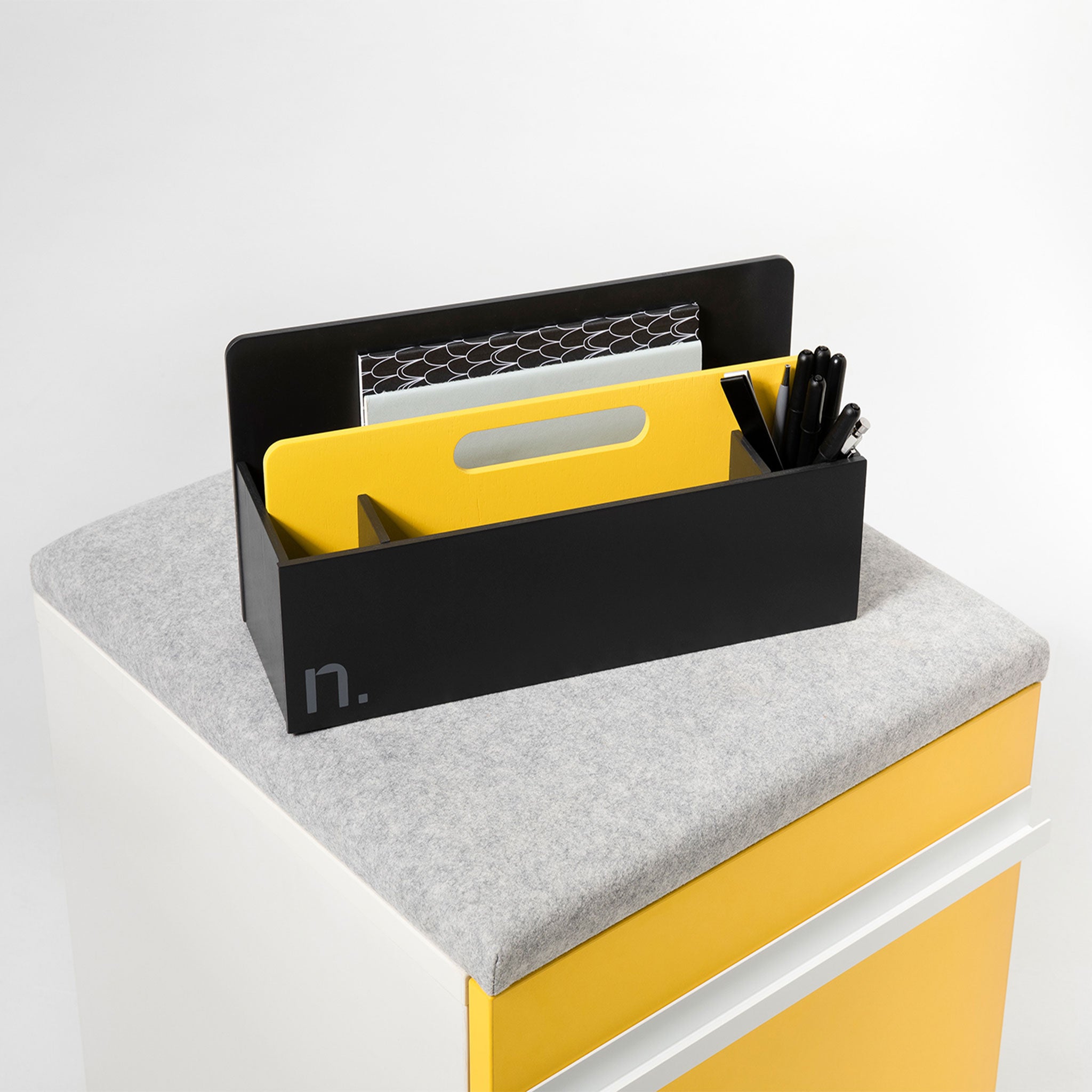 Eine gelbe Toolbox steht auf einem Rollcontainer mit gelber Front und grauem Sitzpolster. In den Fächern der Toolbox sind Stifte und Zettel verteilt.