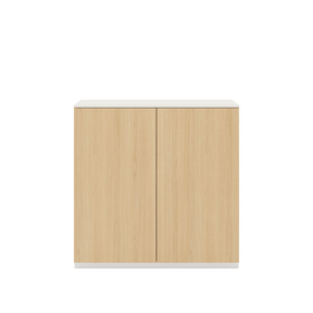 Vor weißem Hintergrund sieht man ein Sideboard aus Eichenholz. Die beiden Drehtüren haben keine Griffe. Auf dem Sideboard ist eine cremeweiße Abdeckplatte angebracht.