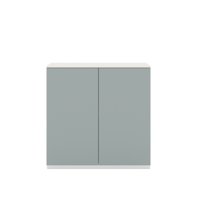 Vor weißem Hintergrund sieht man ein fjordgrünes Sideboard mit zwei Drehtüren. Die Türen haben keine Griffe und sind mit einem Push-to-open-Mechanismus ausgestattet. Auf dem Schrank ist eine cremeweiße Abdeckplatte angebracht.