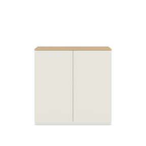 Vor weißem Hintergrund sieht man ein cremeweißes Sideboard mit zwei Drehtüren. Auf dem Schrank ist eine Abdeckplatte aus Eichenholz angebracht.