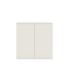 Vor weißem Hintergrund sieht man ein cremeweißes Sideboard mit zwei Drehtüren. Die Türen haben keine Griffe. Auf dem Sideboard ist eine cremeweiße Abdeckplatte angebracht.